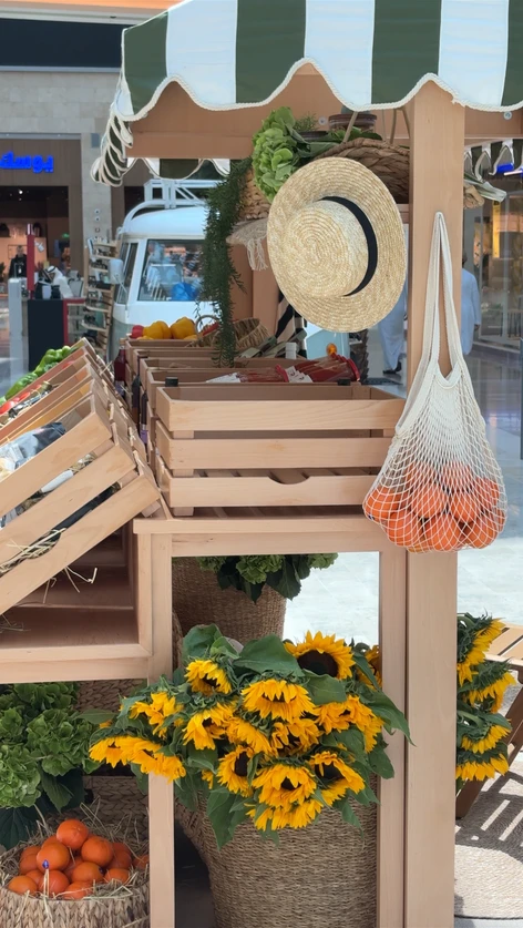 Straw boater hat and net produce bag hanging beside crates of fresh vegetables